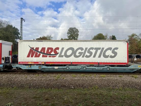 Vorbeifahrender Güterzug mit Containerwagen, auf dem Container steht „Mars Logistics“.