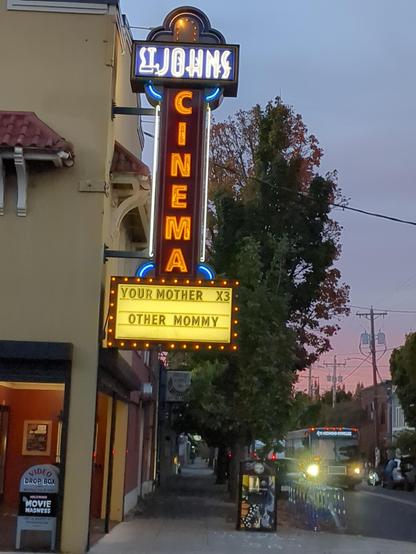 a neon sign that reads st johns cinema. there is a section with swappable letters to show current films. it reads "your mother x3"  and "other mommy" on a newline