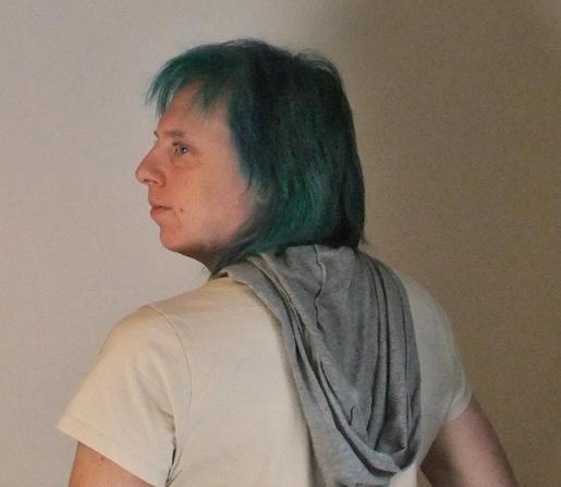 A person looking away from the camera, weiring a beige t-shirt with grey hood draped down their back.
